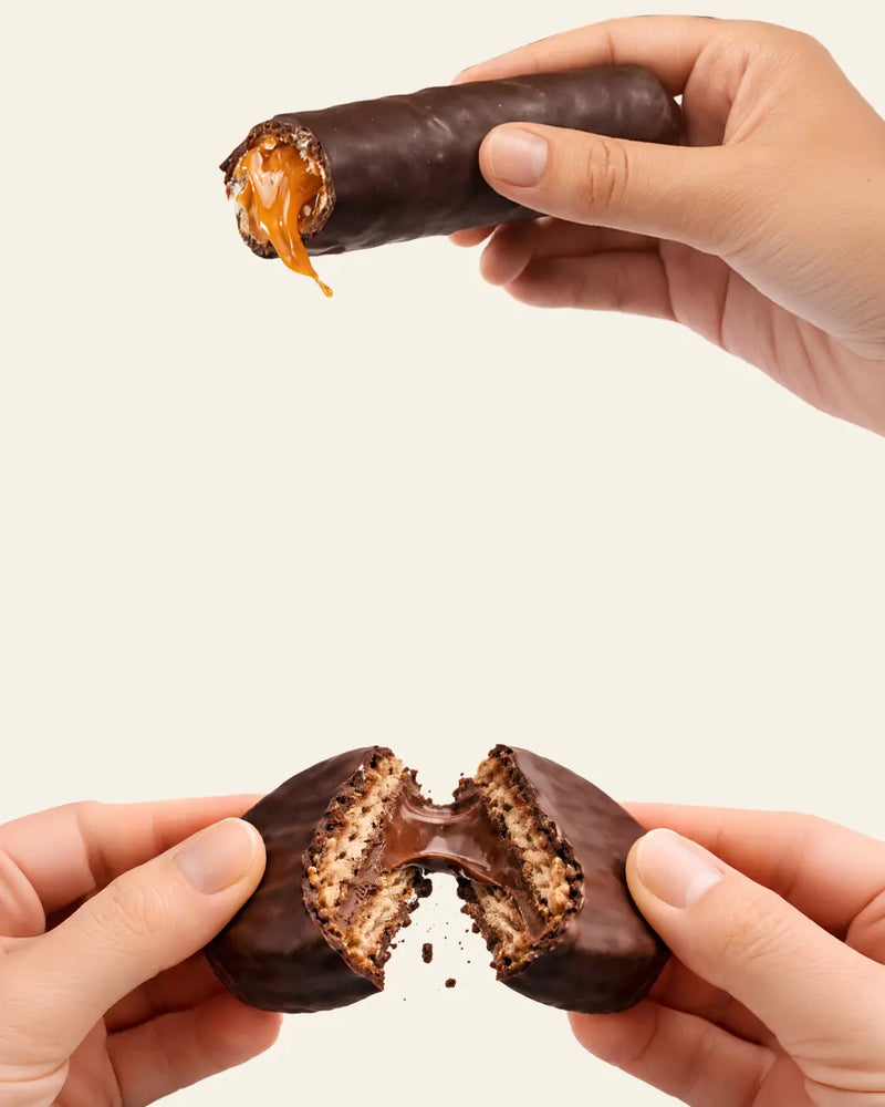 Galleta bañada en chocolate con un mordisco, sostenida con ambas manos sobre un fondo claro.