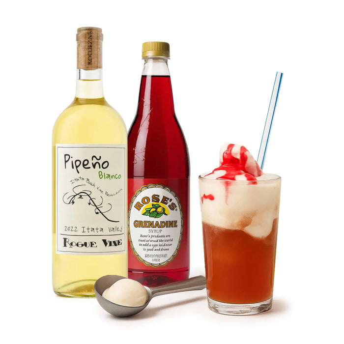Dos botellas de Pipeón Blanco y Rose's Grenadine, un vaso de un cóctel rojo con helado y una pajita, y una cuchara con una sustancia blanca sobre fondo blanco.
